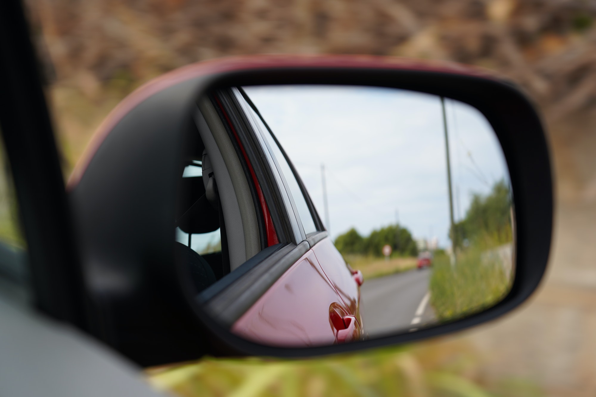 https://dempstersqualitycarcare.com/wp-content/uploads/2023/12/closeup-shot-of-a-rearview-mirror-of-a-red-car-with-the-road-reflection.jpg